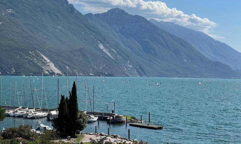 Paesaggio lacustre con barche e montagne verdi sotto un cielo azzurro.